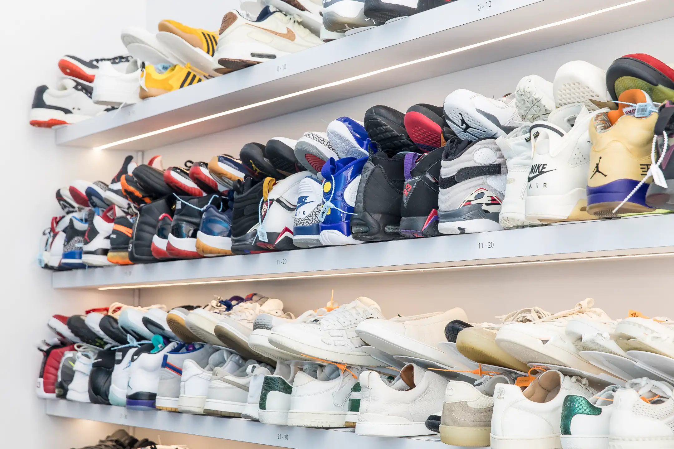 A wall of sneakers organized on illuminated shelves at a Sneakky Klean store.